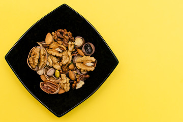 Flat lay ketogenic diet. Walnut,pistachios,pecan and almond in the black square plate on the yellow background. Concept of healthy food.Copy space for mock up