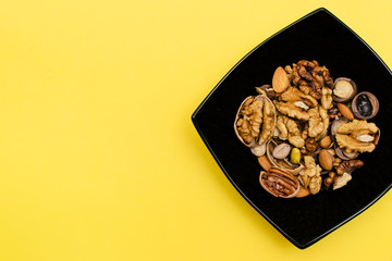 Flat lay ketogenic diet. A mix of walnut,pistachios,pecan,almond in the black square plate on the yellow background. Concept of healthy food.Copy space for mock up