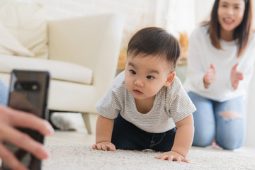 Naklejka premium Portrait of an adorable baby Asian staring and looking at a smartphone There is a mother who is supporting in the background in home.Technology concepts and daily life