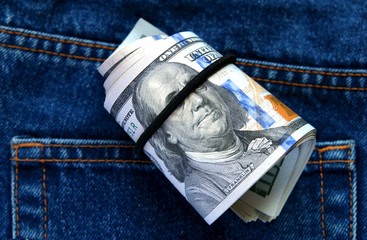 Roll of dollars on the background of blue jeans