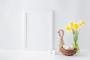 Home interior with easter decor. Mockup with a white frame and yellow daffodils in a glass vase on a light background
