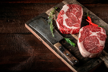 Raw rib eye steak of beef on a wooden Board with a meat cleaver and seasonings