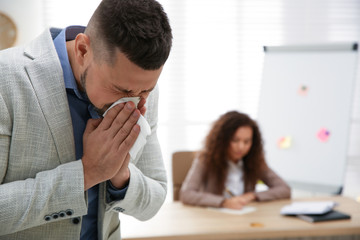 Fototapeta premium Sick man sneezing in office. Influenza virus