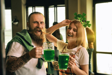 Young woman and man with glasses of green beer in pub. St. Patrick's Day celebration