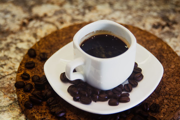 A small cup of espresso and coffee beans on a stand