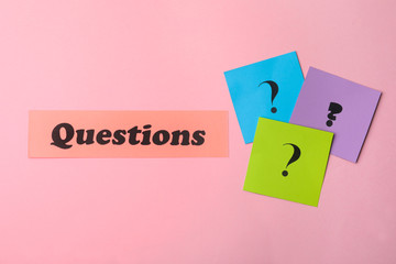 Word QUESTIONS and query marks on pink background, flat lay