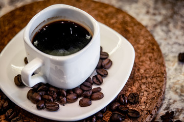 A small cup of espresso and coffee beans on a stand