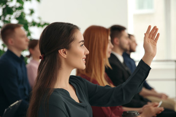 Young woman raising hand to ask question at business training indoors