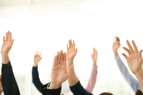 People raising hands to ask questions at business training on light background, closeup