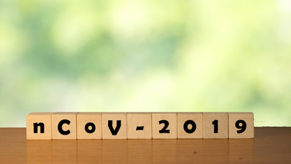 Inscription nCoV 2019 coronavirus on wooden cubes on a green background. Coronavirus background with bokeh nature green color.