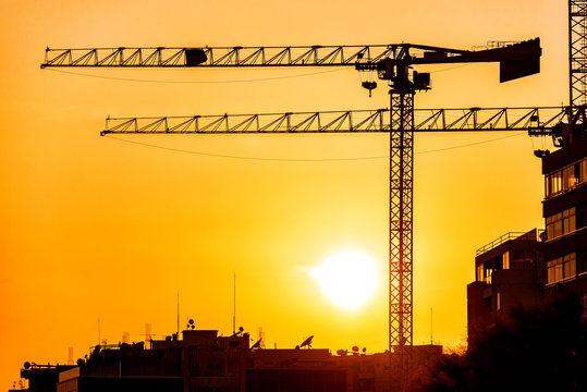 Silhouette of a construction cranes against sunset