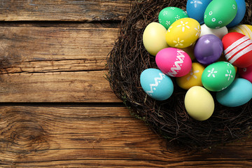 Colorful Easter eggs in decorative nest on wooden background, top view. Space for text