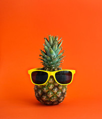 Pineapple on a bright orange background with yellow glasses