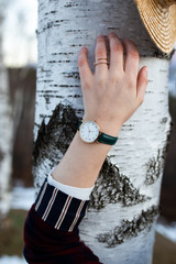 Close up photo of female hand wearing  green watch. She is holding her hand on beautiful white birch tree.