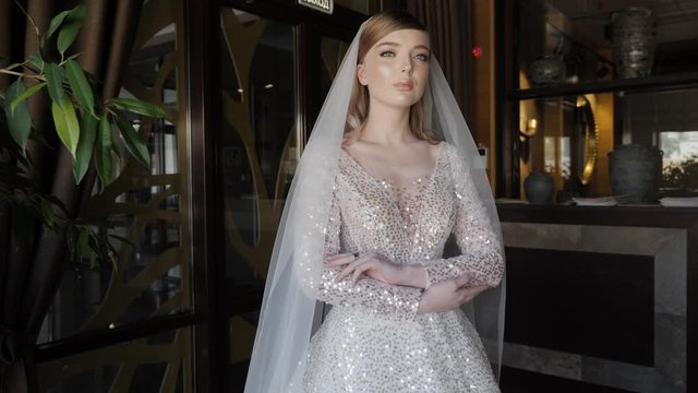 beautiful bride in wedding dress with Swarovski crystals poses for camera standing near restaurant decorations slow motion