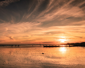 a golden sunset on a sandy beach with the sun reflecting on the wet sands
