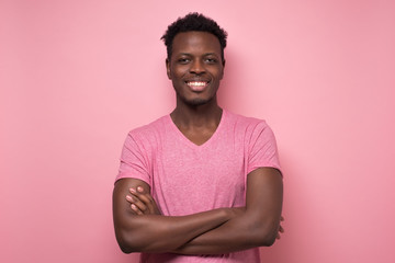 Smiling young african american man with folded hands looking at camera. Studio shot on pink wall