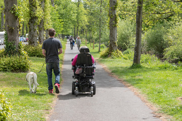 a woman in an electric scooter with her carer walking next to her with a support dog