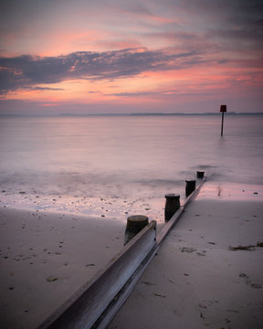 A Pink Sunrise On A Sandy Beach With Calm Water