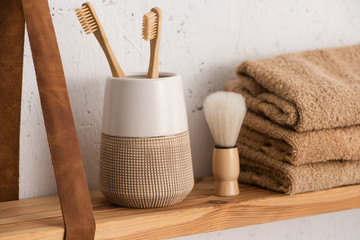 Close up view of shelf with toothbrush holder with toothbrushes, towels and shaving brush in bathroom, zero waste concept