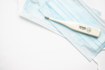 Flat lay protective medical face masks and digital thermometer with high temperature on the white...