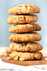 Homemade oat cookies with peanuts and raisins on the kitchen table, blue background. Stack of oatmeal cookies close-up