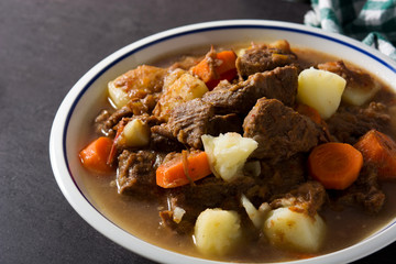 Irish beef stew with carrots and potatoes on black background