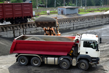 Wheel loader loads gravel into a dump truck at a cargo railway station. Fron-end loader unloads crushed stone in a gravel pit.  Unloading bulk cargo from freight cars on high railway platform © MaxSafaniuk