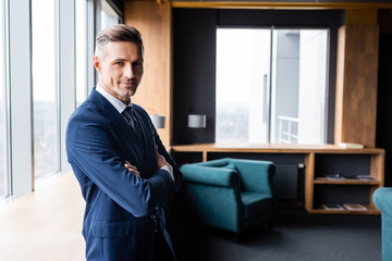 smiling businessman in suit with crossed arms looking at camera in hotel