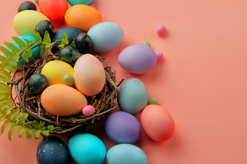 Fototapeta na wymiar Multicolored eggs and lollipops in a nest on a pink background with a sprig of fern, Easter.