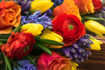 Fototapeta na wymiar Bright spring bouquet of yellow tulips,blue hyacinths,speedwell,red ranunculus and orange roses lying on the brown wooden table.Present concept for Birthday, mother's Day, 8 March.Selective focus