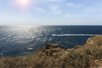 The bright sun on the Cape Tarkhankut. A boat is floating on the sea. Ripples on the water from a strong wind