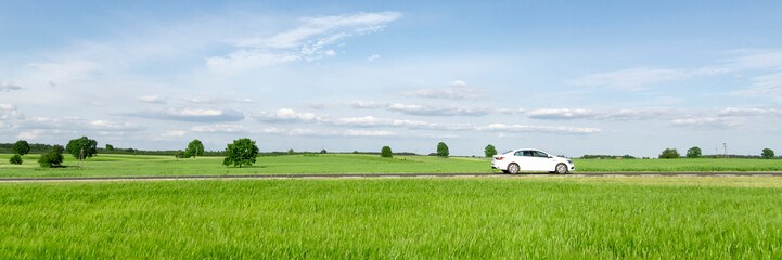 Small passenger car driving through green countryside meadow, on the road trip