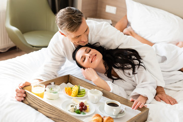 Obraz na płótnie Canvas handsome boyfriend hugging smiling girlfriend near tray with food