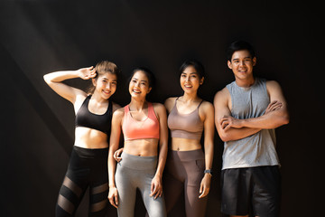 Happy smiling man and women having fun talking in gym. Group of young people relaxing in gym after workout training with black background.