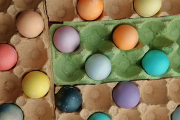 Many colored eggs lie in cardboard trays on a pink background in a checkerboard pattern.