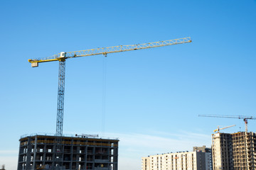 Tower cranes working at construction site against blue sky. Crane lifting a concrete bucket. Construction process of the new residential buildings. Transportation blocks and pouring of the cement mix