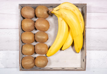 Bananas and kiwis placed in an old wooden tray on a background of old wooden floor