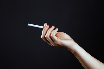 female hand holding a cigarette on a dark background close-up