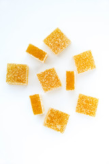 Pineapple, lemon, vanilla pate de fruit (jelly, marmalade, fruit candy) covered with sugar. White background, top view. There are sliced jellies on a photo to show a texture inside of pate de fruit.