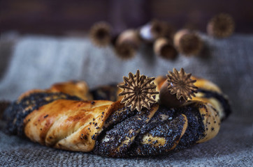 Poppy seed roll on a dark background and burlap with poppy heads
