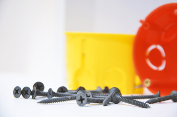 Black screws and a plastic yellow, red box for electrical switches and sockets.