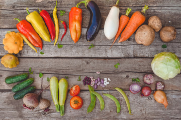 Fresh vegetables: carrots, eggplant, peas in pods, bell peppers, squash, cucumbers, tomatoes, potatoes, onions, beans, cabbage lie on a wooden table ( table top) in a circle, top view. Photo.