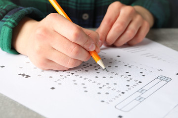 Young woman fills test sheet on grey table, close up