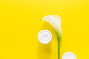 Natural face cream and beautiful white Calla Lily on bright yellow background. Face care concept. Minimalism style composition