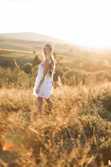 Beautiful young boho hippie girl in white dress at sunset, smiling and having fun. Feathers in hair, bohemia boho style