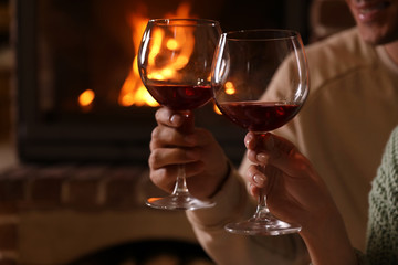 Lovely couple with glasses of wine near fireplace indoors, closeup. Winter vacation