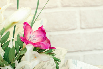 Gentle spring bouquet of white roses,white irises,lilac and freesia in gift wrapping on white brick background.Present concept for Valentine's Day,Birthday, wedding,mother's Day.Copy space for mock up