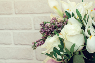 Gentle spring bouquet of white roses,white irises,lilac and freesia in gift wrapping on white brick background.Present concept for Valentine's Day,Birthday, wedding,mother's Day.Copy space for mock up