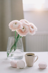 Spring home decor. Cup of coffee and pink rose flowers in vase in morning light. Good morning concept. Interior design of room 